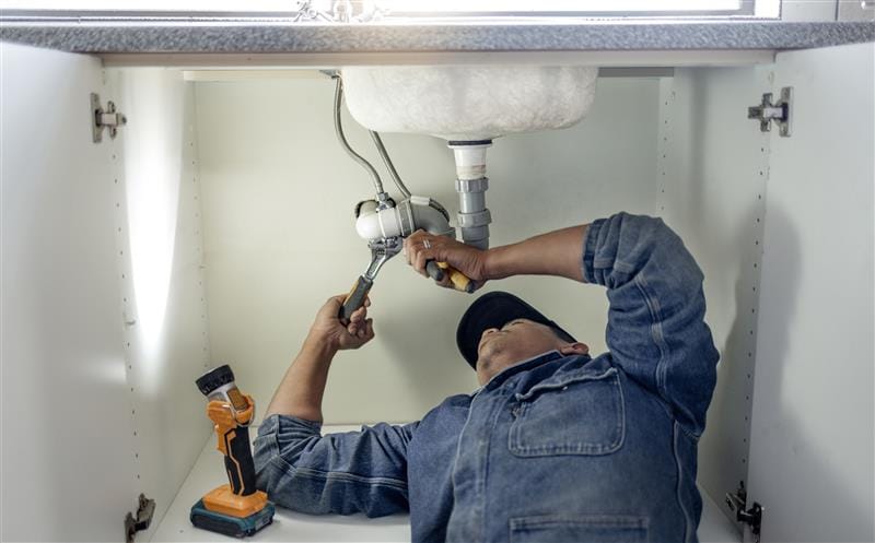 Plumber repairing pipes beneath a bathroom sink in Desert Hot Springs