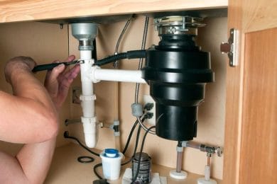 Plumber repairing a garbage disposal beneath a kitchen sink in Desert Hot Springs