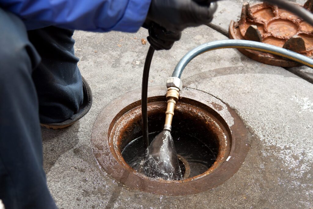 Plumber hydro jetting a sewer line through a manhole in Desert Hot Springs