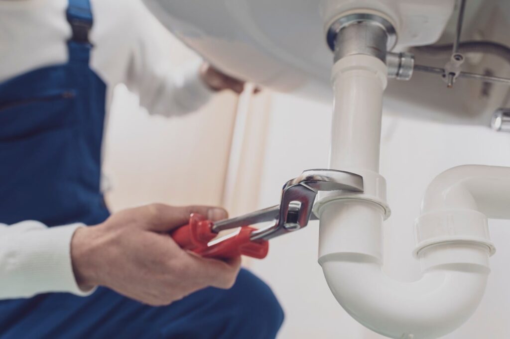 Plumber repairing a white drain pipe beneath a sink in Desert Hot Springs