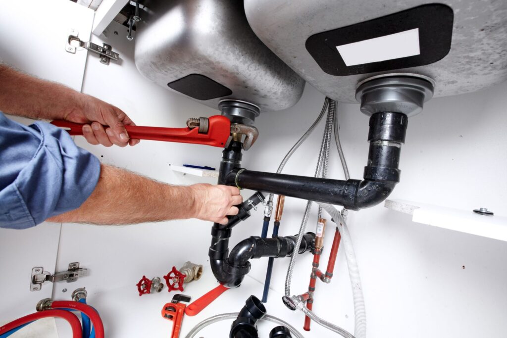 Plumber repairing drain pipes beneath a kitchen sink in Desert Hot Springs